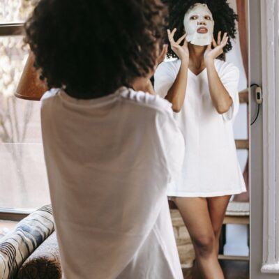 African American woman with sheet mask looking in mirror