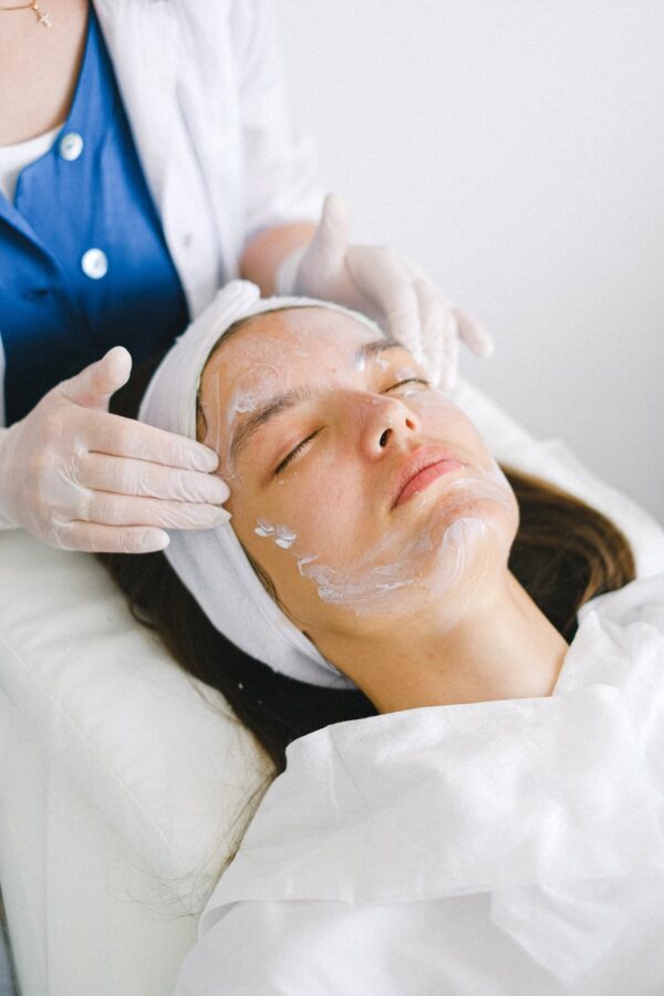 Crop beautician massaging client face with lotion during spa procedures